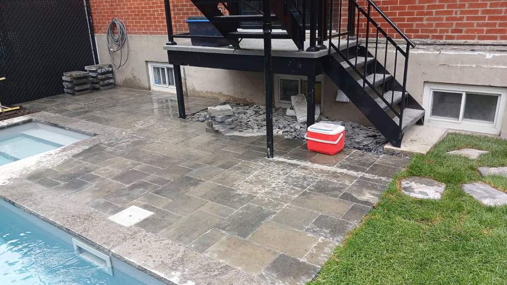 Aménagement de pavé uni gris foncé autour d’une piscine résidentielle avec escalier extérieur métallique